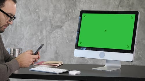 Man Using Smartphone in front of Green Screen Computer