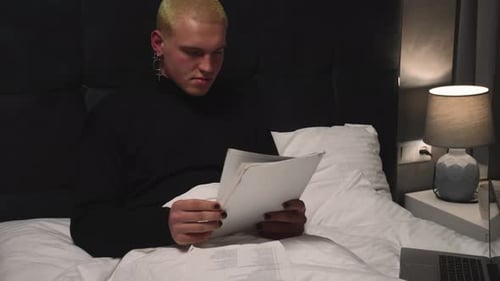 Young Adult Reviews Documents in Bed at Night