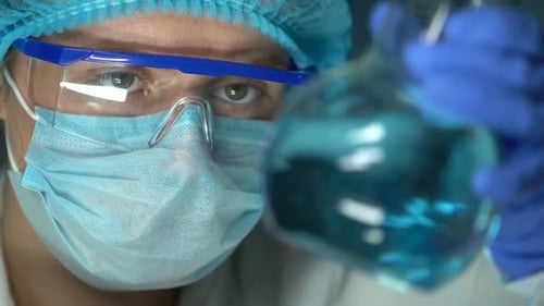 Expert de laboratoire tenant le flacon avec le liquide transparent bleu, contrôle de la qualité