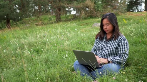 Asian woman sitting and working on laptop in a farm