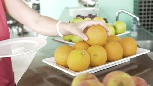 Beim Frühstück frisches Obst auf den weißen Teller legen