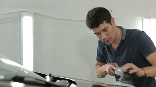 Man Polishing Black Car with Power Buffer in Garage