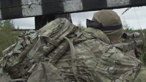 Camouflaged Soldier Aims Weapon in Rural Environment