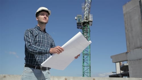 Construction Manager Look At The Sheet With Plan Of Building Under Construction