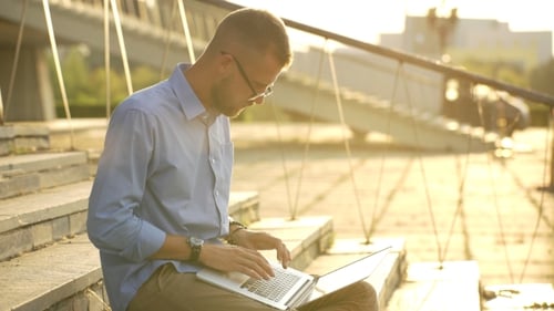 Happy Student Browsing The Internet On His Laptop And Sitting Outdoor
