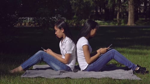 Women Using Phones Back to Back in Park