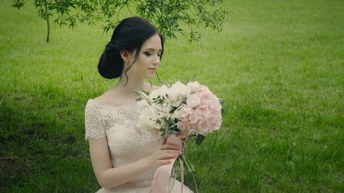 Beautiful Bride with Bouquet Sitting on Green Grass