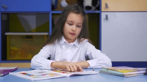 Cute Little Girl Studying At The Library Doing Homework And Smiling