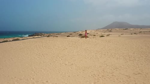 Woman Stands on Sandy Dune Near Ocean