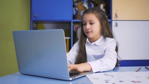 SchoolGirl Studying At The Library Doing After Lessons Homework With Laptop PC. Elementary School