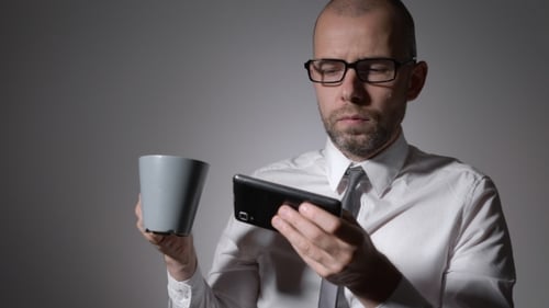 Man Looking at Phone and Drinking Coffee