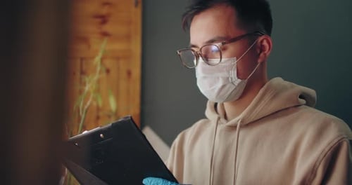 Young Adult Writing on Clipboard Wearing Mask