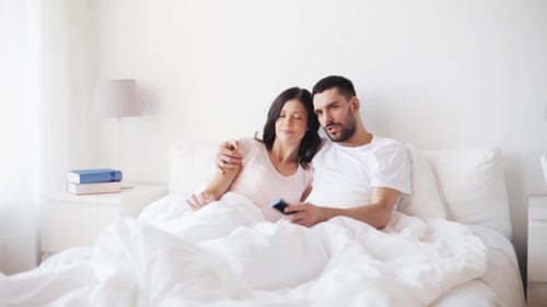 Happy Couple Watching Tv In Bed At Home