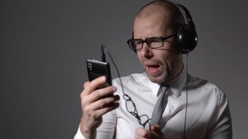 Homme d'affaires en chemise et gros écouteurs, chantant dans un smartphone, utilise une application.