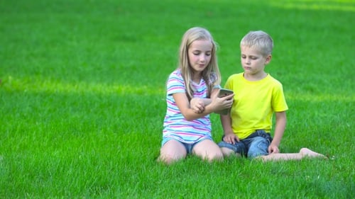 Girl and Boy Watching Smartphone on Green Grass