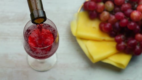 Pouring Red Wine Next to Cheese and Grapes