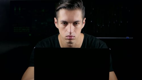 Male Hacker Working On a Computer In a Dark Office Room