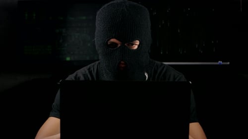Dangerous Hacker In a Mask Working On a Computer In a Dark Office Room