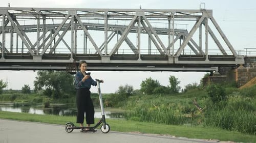 Woman Stands With Scooter And Looks At Phone