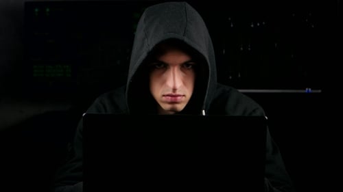 Hacker In a Hooded Working On a Computer In a Dark Office Room