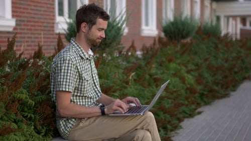 Man Works on Laptop Outside in Suburban Setting