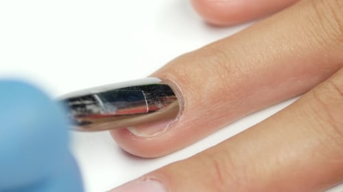 Der
Manikürist arbeitet mit einem Spatel auf den Nagel und drückt die Nagelhaut zurück.