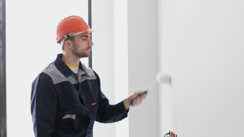 Young adult paints white wall indoors