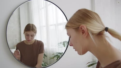 Young Woman Applying Lotion to Face in Bathroom