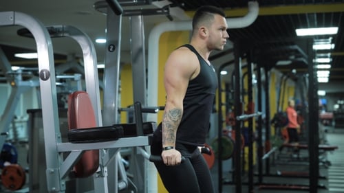 Side View Of Young Muscular Man Doing Exercise At The Gym