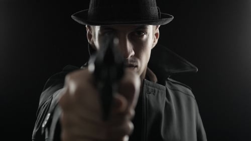 Gangster mit Hut und schwarzem Umhang. Mafioso zielt mit einer Waffe auf
die Kamera