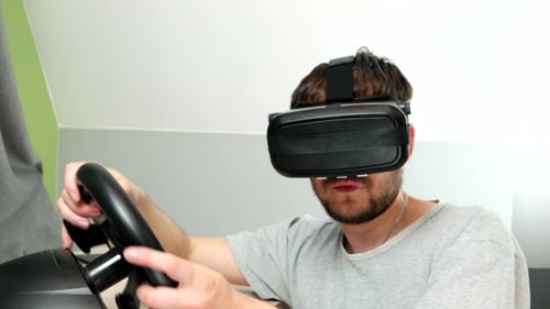 Mann spielt begeistert in Virtual-Reality-Brillen, fährt einen Autosimulator.