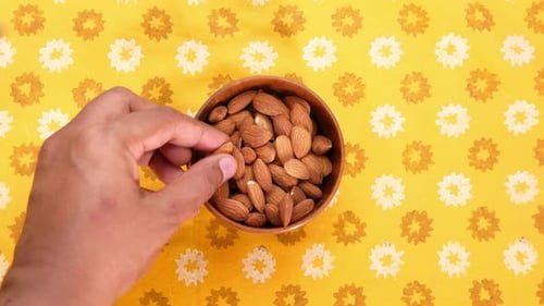 Top View of Person Hand Picking Almond Nuts From a Bowl