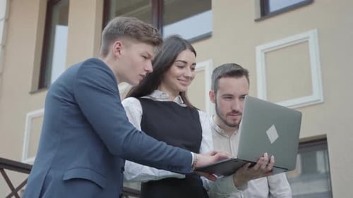 Junge Frau und zwei Männer in formeller Kleidung diskutieren Projekt auf dem Laptop auf der Terrasse.
Business