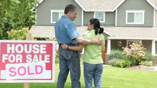 Couple look at new home, SOLD sign in foreground