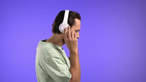 Handsome Young Man Enjoy Music Smiling with Headphones in Studio Against Violet Background