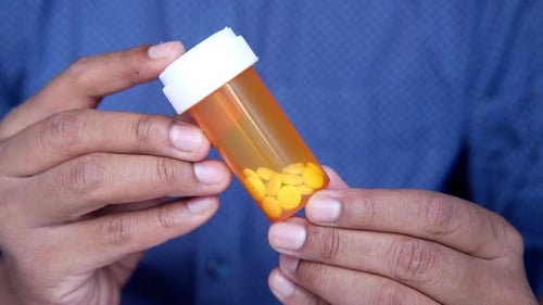 Person Shaking Bottle of Yellow Prescription Pills
