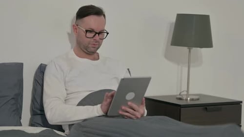 Man Using Tablet in Bed at Home