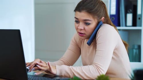 Busy office girl talking on phone and typing on laptop