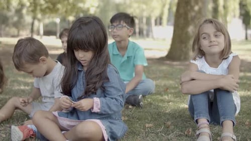 Multiethnic Girls and Boys Sitting on Grass in Park Together