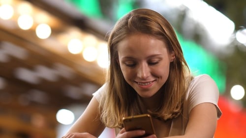Cheerful pretty young woman texting to her boyfriend on smartphone.