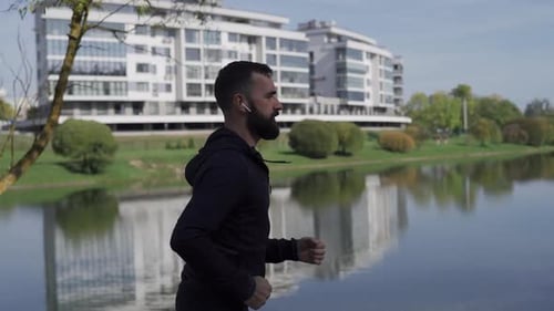 Adult Man Runs in the Park Near the City Camera Following Runner in Wireless Headphones Healthy