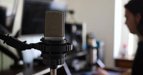 A male music producer at his music recording studio desk with a condenser microphone for recording a