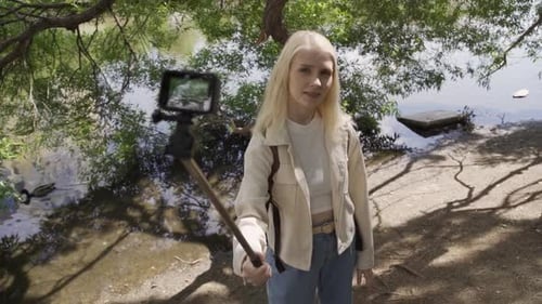 Blonde Woman Recording Vlog By Lake With Selfie Stick