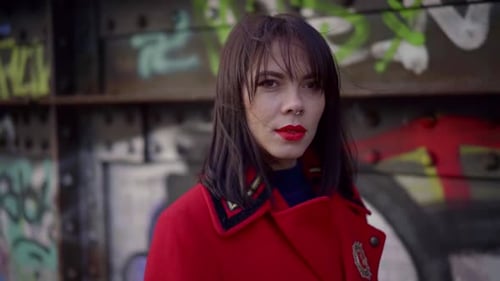 Close-up Portrait of a Dark-haired Young Pretty Girl Walking Against a Wall with Graffiti