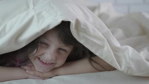 Smiling Child Lying in Bed Under White Sheet