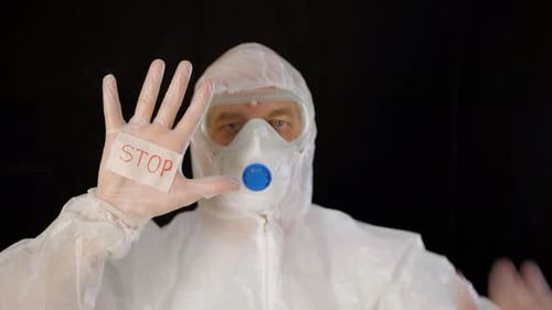 Virologe in weißem Schutzanzug, Maske und Handschuhen zeigt Stopvirus auf schwarzem Hintergrund
