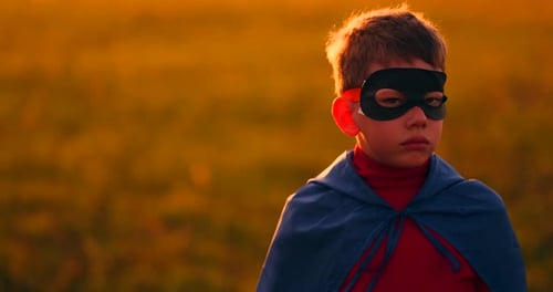The Boy in the Mask and Cape of a Super Hero at Sunset in a Field
