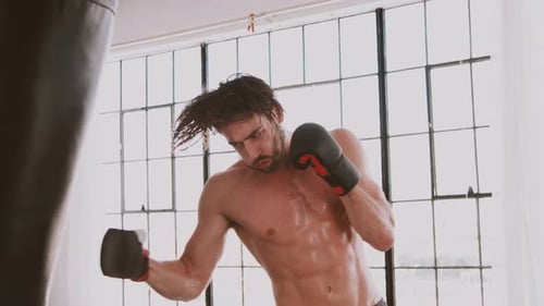 Muscular Man Training with Punching Bag in Bright Gym