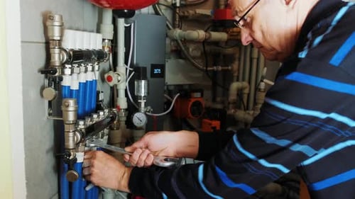 Adult Working on Pipes with Wrench Near Boiler