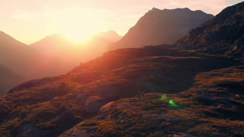 Aerial: couple backpackers hiking to the mountain top, rocky mountain peak in backlight